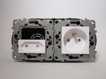 Two frames screwed into a double wall box, the left one has only a non-earthed socket which is placed sideways, the right one has an earthed socket.