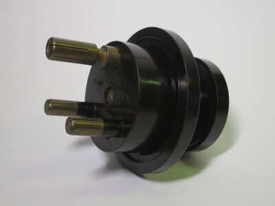 Front view of the plug. It's made of dark brown bakelite and has three round pins. The L and N pins have protective sleeving.